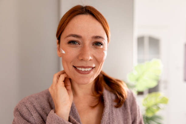 istock Smiling woman applying moisturizer cream on her face 2191394938
