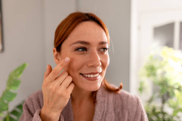 istock Smiling woman applying face cream looking in the mirror 2191394963