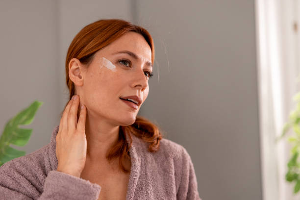 istock Woman applying moisturizer cream on face looking in the mirror 2191395015