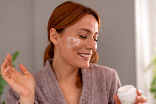 istock Smiling woman applying moisturizer cream on her face in heart shape 2191395210