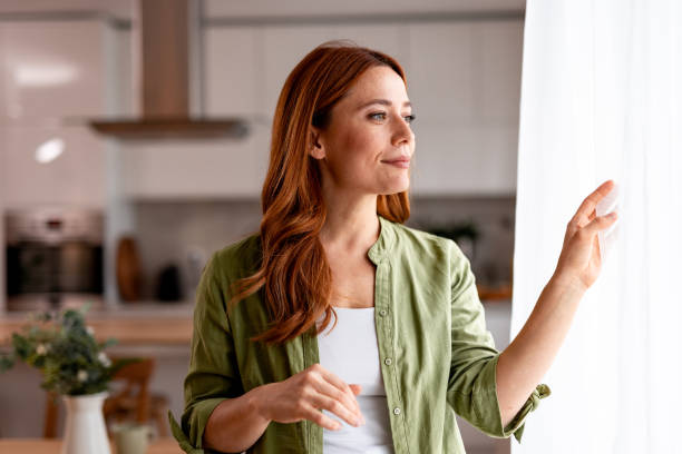 istock Woman looking through the window enjoying sunlight in her modern apartment 2191395476
