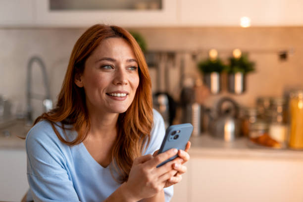istock Woman Holding Smartphone and Smiling in a Modern Kitchen Setting 2191395494