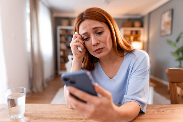 istock Concerned Woman Checking Her Mobile Phone While Sitting in a Cozy Home Setting 2191395538