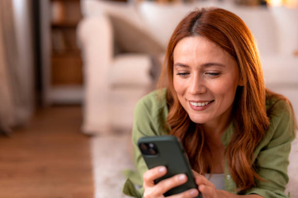 istock Smiling woman using smartphone lying on the floor at home 2191395555