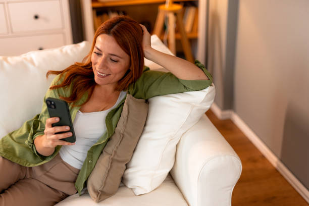 istock Smiling woman relaxing on sofa using smartphone at home 2191395599