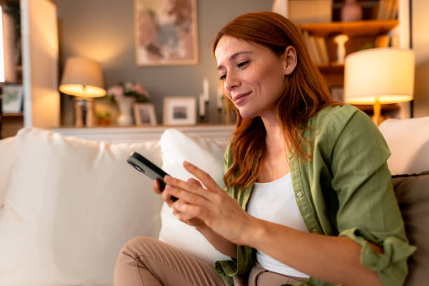 istock Young woman using mobile phone while relaxing on sofa at home 2191395674