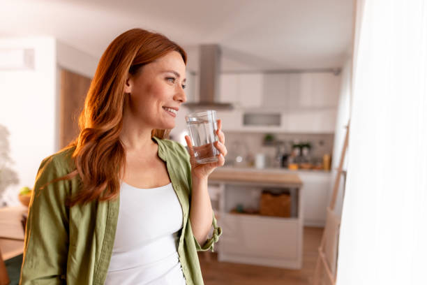 istock Smiling Woman Drinking Water in Kitchen by Window 2191395782