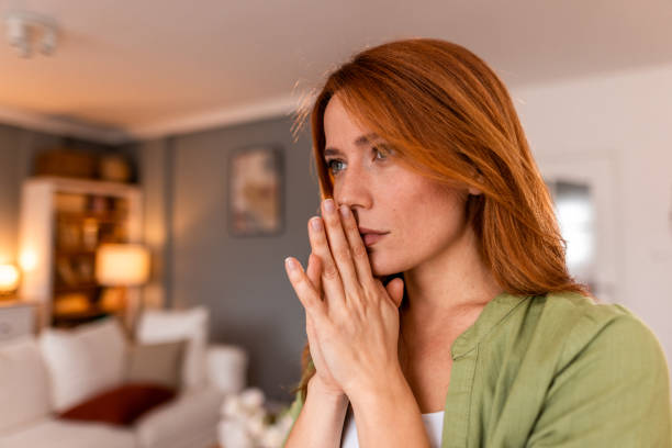 istock Pensive young woman looking away with hands clasped at home 2191395959