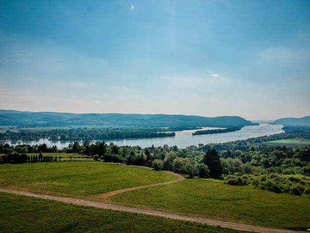 The winding Danube river flows through a picturesque landscape, surrounded by vibrant green fields and rolling hills. The bright blue sky enhances the serene atmosphere of the famous Danube bend.