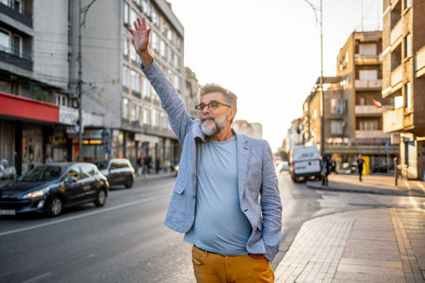 Homem maduro chamando táxi na rua da cidade Homem maduro alegre acenando para pegar um táxi na cidade homem chamando táxi fotos de stock, fotos e imagens sem direitos autorais