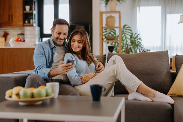 istock Happy couple relaxing on sofa and using smartphone at home 2191402252