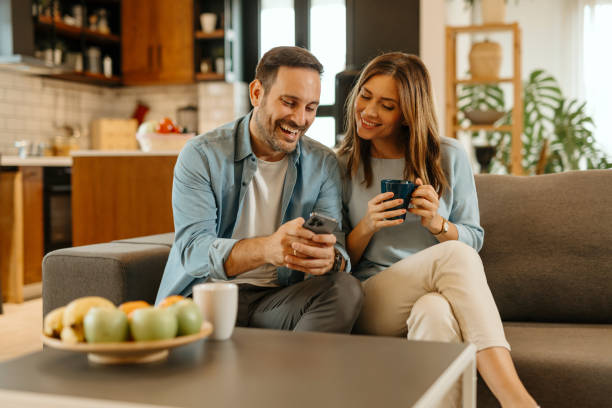 Happy couple relaxing on sofa, browsing social media and drinking coffee