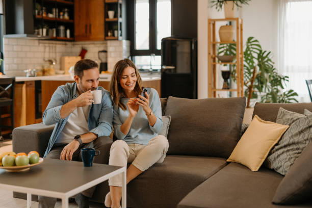 istock Couple relaxing on sofa, drinking coffee and using smartphone in living room 2191402279