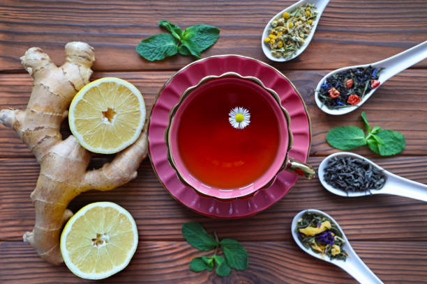 Herbal Tea with Ginger, Lemon, and Loose Leaf Blends. A vibrant composition featuring a red teacup filled with herbal tea, surrounded by fresh ginger, lemon slices, mint leaves.