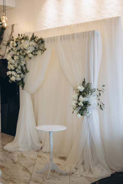 istock Elegant white wedding decorations with floral arrangements and white curtain backdrop 2191407565