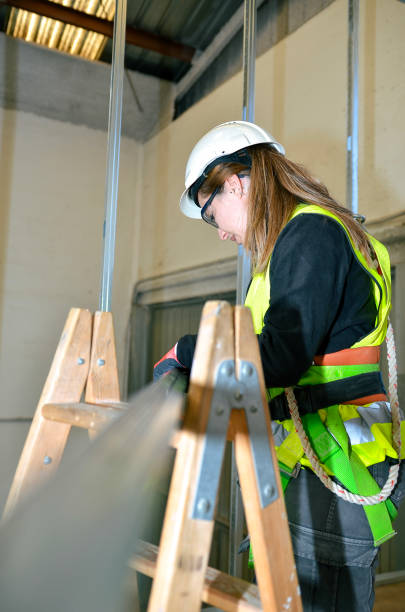 Woman working on a construction site, installing plasterboard while standing on a wooden ladder