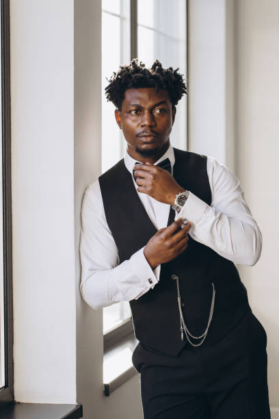 istock Elegant groom adjusting bow tie and cufflinks near window 2191407860