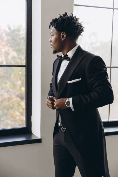 istock Elegant groom adjusting his suit while looking out the window 2191408012