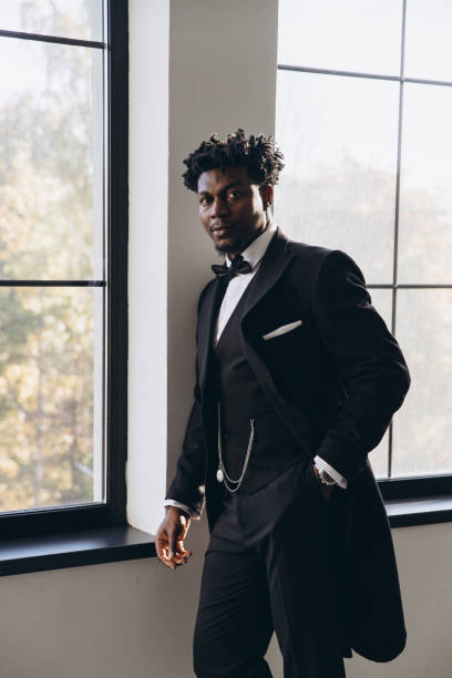 istock Elegant groom wearing black suit posing near window 2191408013