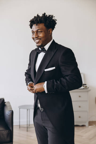 istock Elegant groom getting ready, buttoning his black tuxedo and smiling 2191408054