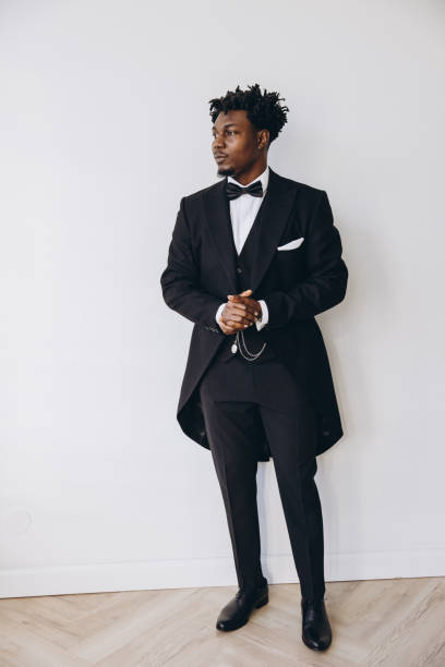 istock Elegant groom wearing black tailcoat posing in white room 2191408114