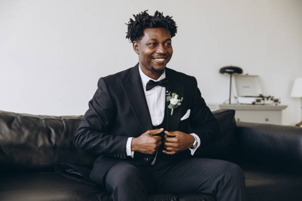istock Elegant groom adjusting his suit while sitting on a sofa 2191408493