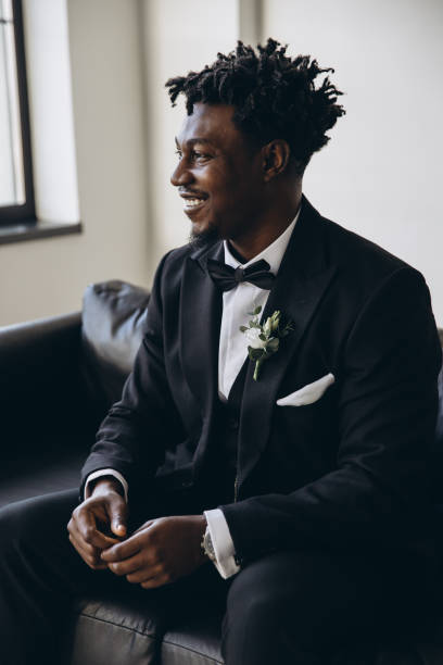 istock Elegant groom wearing black suit sitting on sofa waiting for bride 2191408518