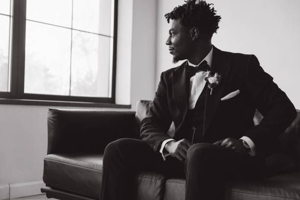 istock Groom sitting on sofa looking out window in black and white 2191408521