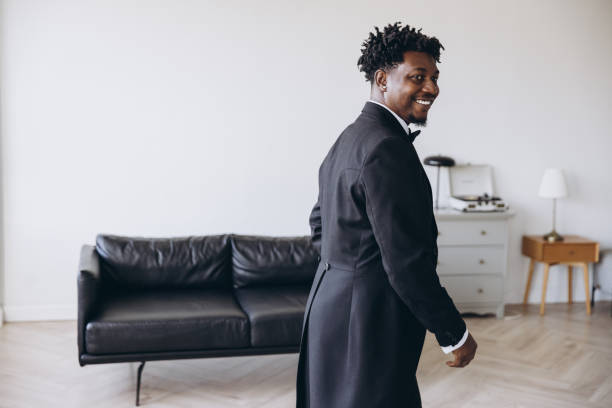 Groom wearing elegant tailcoat smiling and walking in modern apartment