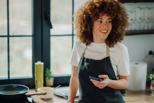 istock Woman wearing apron using smartphone in kitchen and smiling 2191409439