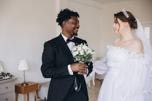 istock Groom holding bouquet smiling at bride during interracial wedding ceremony 2191409726
