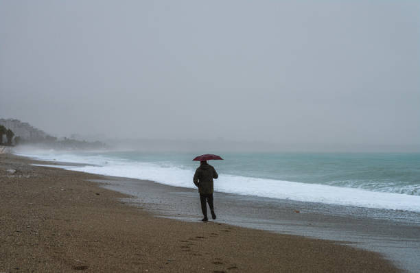 Lonely man walking on the beach on a rainy day
