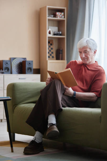 istock White Haired Senior Man Reading Book Sitting on Sofa at Home 2191411085