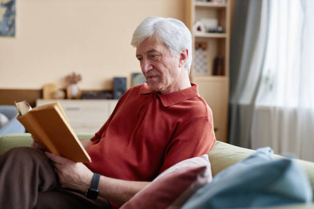 istock White Haired Senior Man Reading Book Sitting on Couch 2191411110