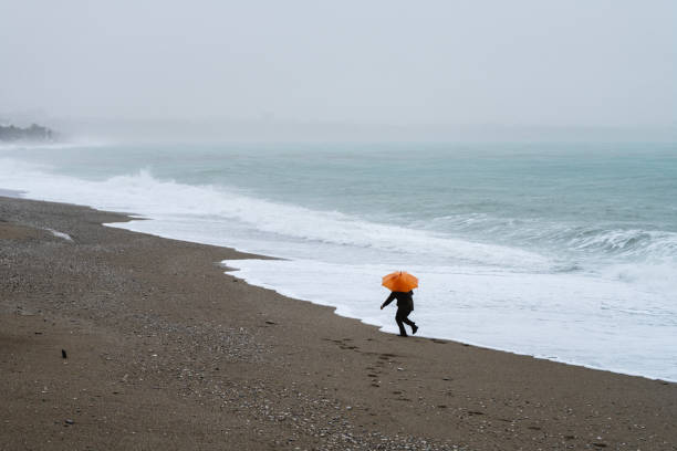 istock Lonely man walking on the beach on a rainy day 2191411196