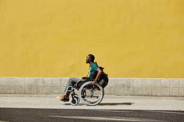 istock Black Man using Wheelchair in Sunlight Against Yellow Wall 2191411525