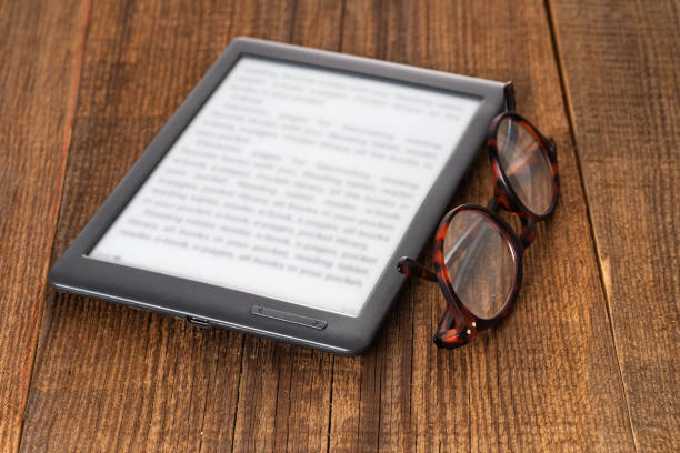 e-book reader and glasses on a wooden table.