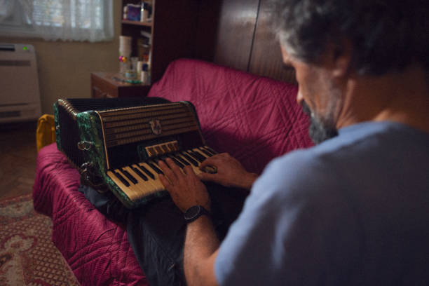 Family moments at home. Father has fun while playing music on accordion in a funny way surrounded by homey items and soft light. Love and sharing time.