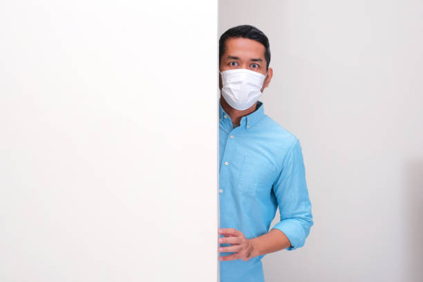 istock A man wearing medical face mask peeking behind a wall with shocked expression 2191424508