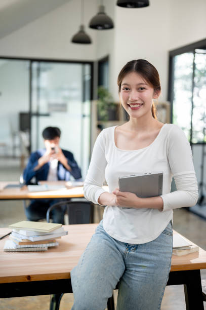 istock A beautiful Asian student holding her tablet and smiling at the camera while standing in a library. 2191425748