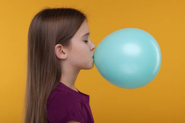 istock Girl inflating bright balloon on orange background 2191427859