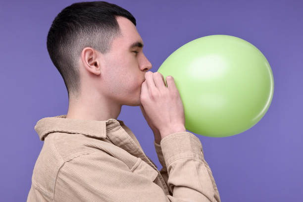 istock Young man inflating light green balloon on purple background 2191428696