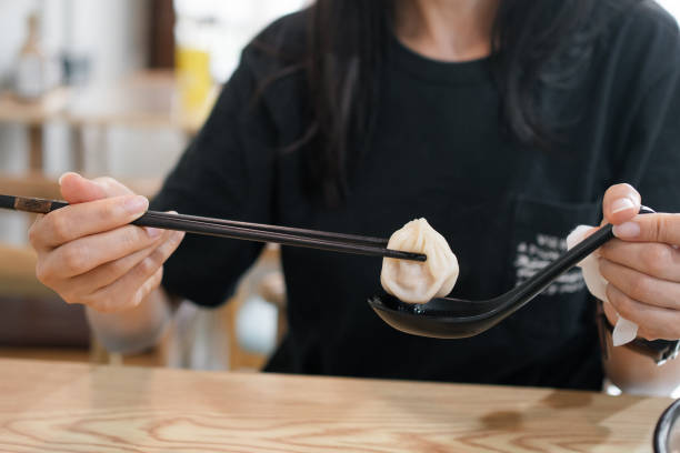 istock Hand using chopsticks to place a dumpling on a spoon filled with soup, ready to eat. 2191429130