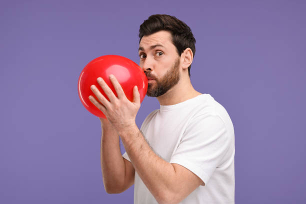 istock Man inflating red balloon on purple background 2191429270