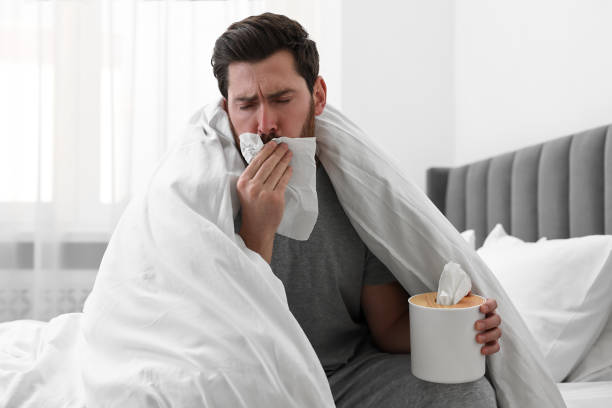 istock Sick man with tissue coughing on bed at home. Cold symptoms 2191429421