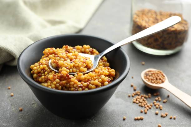 istock Whole grain mustard in bowl, spoon and dry seeds on grey table 2191432616