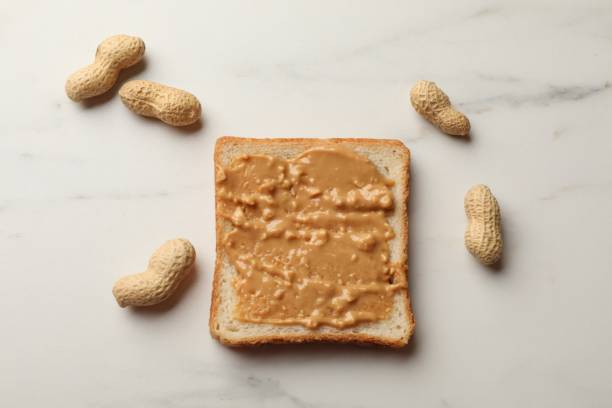 istock Delicious toast with peanut butter and nuts on white marble table, flat lay 2191433498