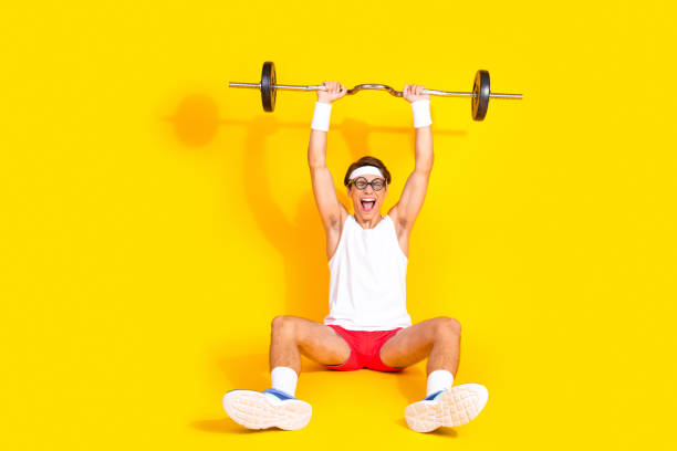 istock Happy young man lifting weights while sitting on the floor, surrounded by a vibrant yellow background, embodying joy and fitness 2191444467
