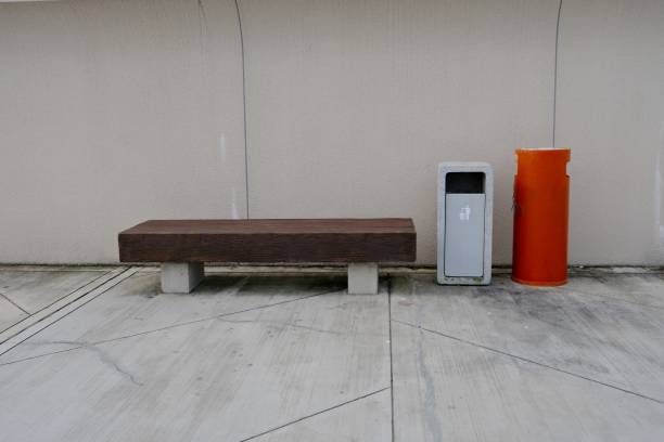 istock Minimalist outdoor bench with a trash bin and an orange cylinder against a plain wall 2191447949