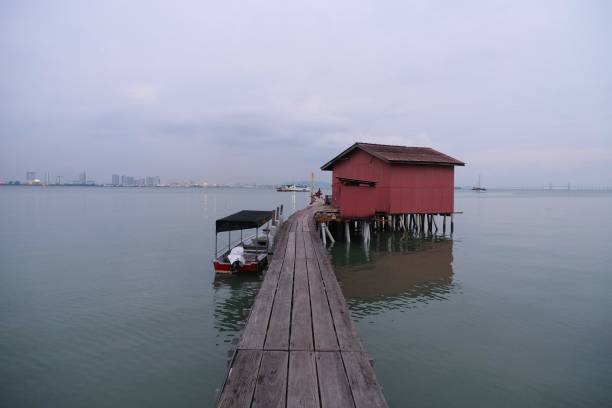 istock Rustic wooden stilt house with a connecting pier over calm waters, surrounded by a tranquil sea and distant cityscape. 2191447993